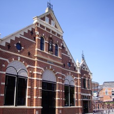 Historisches Backsteingebäude mit Rundbogenfenstern und weißen Zierelementen unter klarem Himmel.
