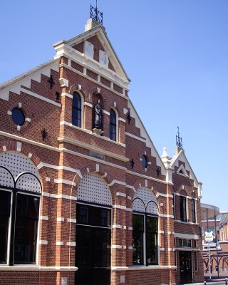 Historisches Backsteingebäude mit Rundbogenfenstern und weißen Zierelementen unter klarem Himmel.