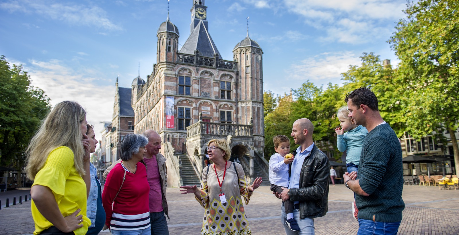 Gids geeft een rondleiding aan een groep mensen op een plein voor een historisch stadhuis in Nederland.