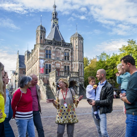 Gids geeft een rondleiding aan een groep mensen op een plein voor een historisch stadhuis in Nederland.