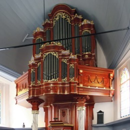 Een imposant kerkorgel met houten details en goudaccenten boven een preekstoel in een lichte kerk.