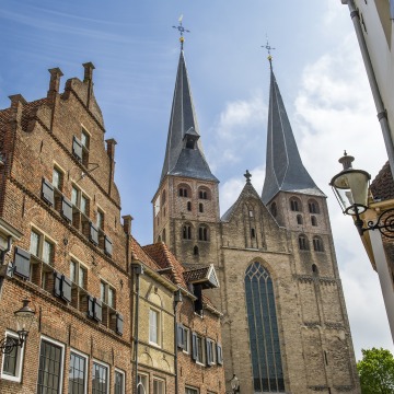 Historische straat in Nederland met bakstenen huizen en een imposante kerk met twee hoge torens.