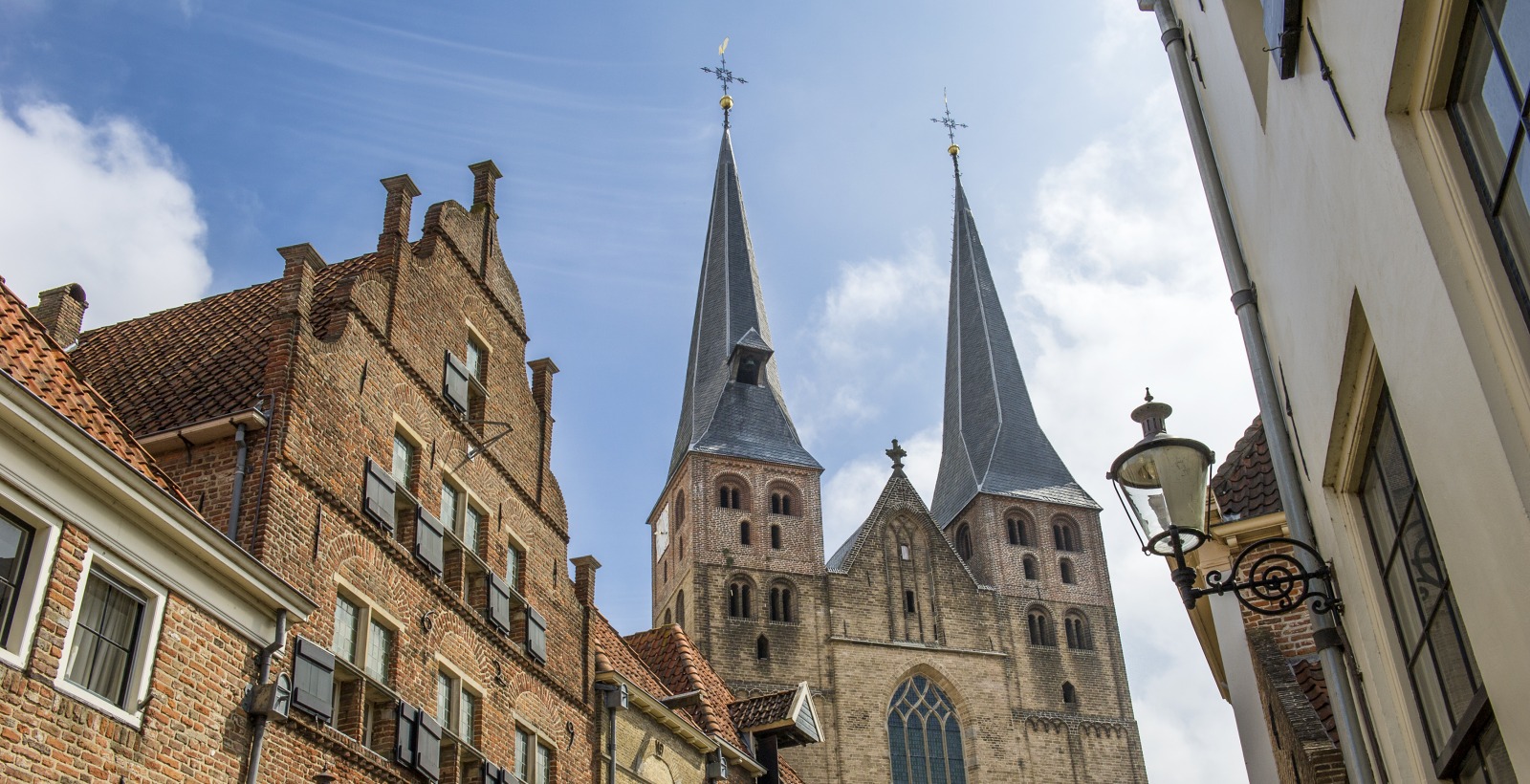 Historische straat in Nederland met bakstenen huizen en een imposante kerk met twee hoge torens.