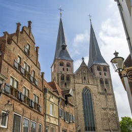 Historische straat in Nederland met bakstenen huizen en een imposante kerk met twee hoge torens.