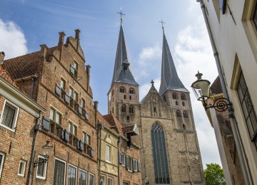 Historische straat in Nederland met bakstenen huizen en een imposante kerk met twee hoge torens.