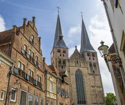 Historische straat in Nederland met bakstenen huizen en een imposante kerk met twee hoge torens.