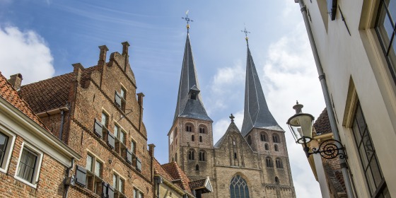 Historische straat in Nederland met bakstenen huizen en een imposante kerk met twee hoge torens.