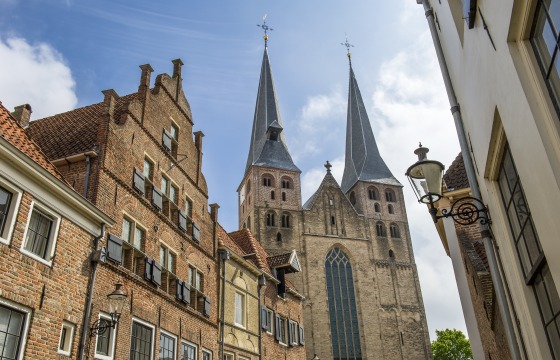 Historische Straße in den Niederlanden mit Backsteinhäusern und einer Kirche mit zwei markanten Türmen.