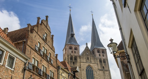 Historische straat in Nederland met bakstenen huizen en een imposante kerk met twee hoge torens.