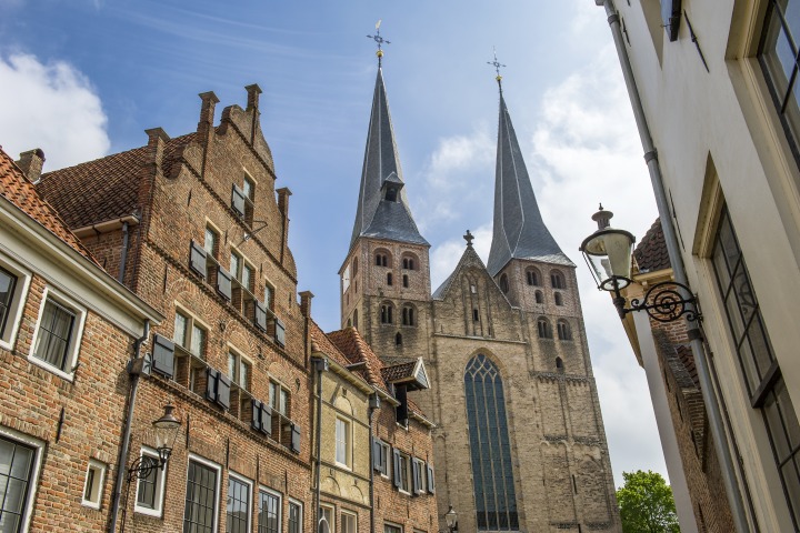 Historische Straße in den Niederlanden mit Backsteinhäusern und einer Kirche mit zwei markanten Türmen.