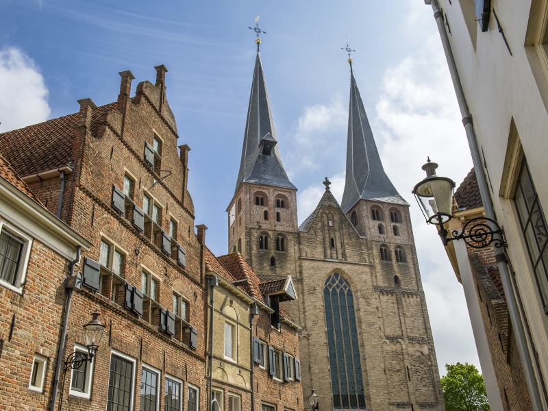 Historische straat in Nederland met bakstenen huizen en een imposante kerk met twee hoge torens.