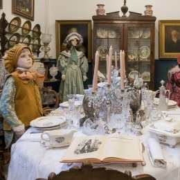 Antieke eetkamer met poppen in Victoriaanse kleding, gedekte tafel en porseleinen servies in museum.