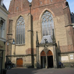 Vooraanzicht van een historische kerk met hoge glas-in-loodramen, gotische details en een klokkentoren.