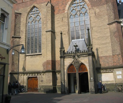 Vooraanzicht van een historische kerk met hoge glas-in-loodramen, gotische details en een klokkentoren.