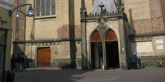 Vooraanzicht van een historische kerk met hoge glas-in-loodramen, gotische details en een klokkentoren.
