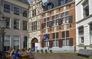 Buitenaanzicht van een historisch gebouw met terras en mensen die genieten op een zonnige dag in Nederland.