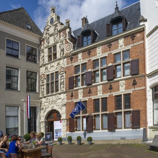 Buitenaanzicht van een historisch gebouw met terras en mensen die genieten op een zonnige dag in Nederland.