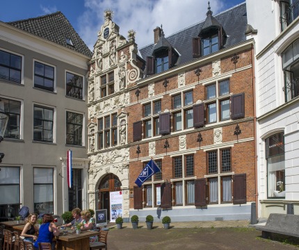 Buitenaanzicht van een historisch gebouw met terras en mensen die genieten op een zonnige dag in Nederland.