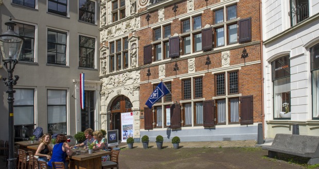 Buitenaanzicht van een historisch gebouw met terras en mensen die genieten op een zonnige dag in Nederland.