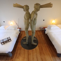 Twee aparte bedden met een groot kunstbeeld van twee figuren met trechterhoofden in het midden.