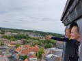Twee meisjes kijken glimlachend naar buiten en wijzen vanaf een hoge toren over een Nederlands stadje.