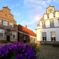 Oude Nederlandse herenhuizen met trapgevels en bloembedden op een geplaveid dorpsplein bij zonsondergang.