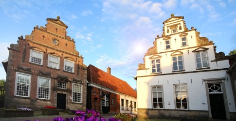 Oude Nederlandse herenhuizen met trapgevels en bloembedden op een geplaveid dorpsplein bij zonsondergang.