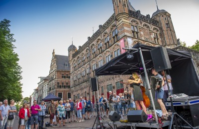 Straatoptreden van muzikanten voor een historisch gebouw met toeschouwers in de avondzon.