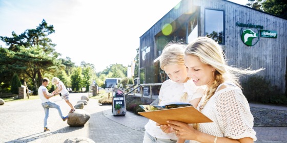Moeder en dochter lezen samen een gids buiten bij het bezoekerscentrum met museum, zonnige dag.