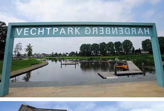 Kunstinstallatie met blauw frame en tekst 'Vechtpark Hardenberg' bij een waterweg en stedelijke omgeving.