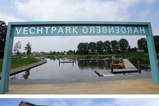 Kunstinstallatie met blauw frame en tekst 'Vechtpark Hardenberg' bij een waterweg en stedelijke omgeving.
