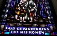 Gebrandschilderd raam met Jezus die kinderen zegent en de tekst: LAAT DE KINDERKENS TOT MIJ KOMEN.