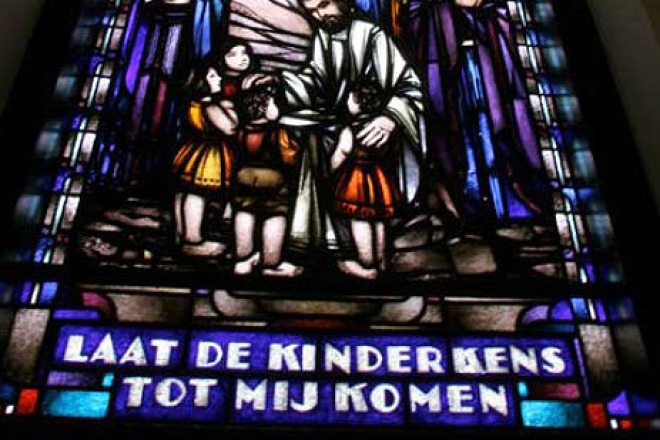 Gebrandschilderd raam met Jezus die kinderen zegent en de tekst: LAAT DE KINDERKENS TOT MIJ KOMEN.