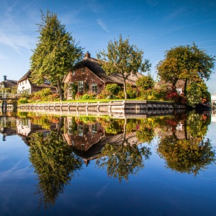 Schilderachtig dorp met huizen, bomen en een brug langs het water met perfecte reflectie in Giethoorn.