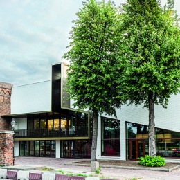 Moderne witte gevel van een gebouw met grote ramen, twee bomen ervoor en een bakstenen muur links.
