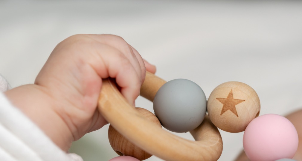 Een babyhandje houdt een houten rammelaar vast met gekleurde kralen, waaronder een met een ster.