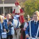 Sinterklaas arriveert te paard tijdens een feestelijke optocht met een fanfare in blauwe uniformen.