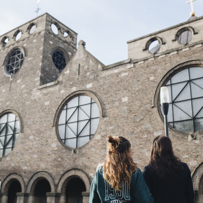 Twee mensen staan buiten en kijken naar een historische kerk met ronde ramen en bakstenen gevel.