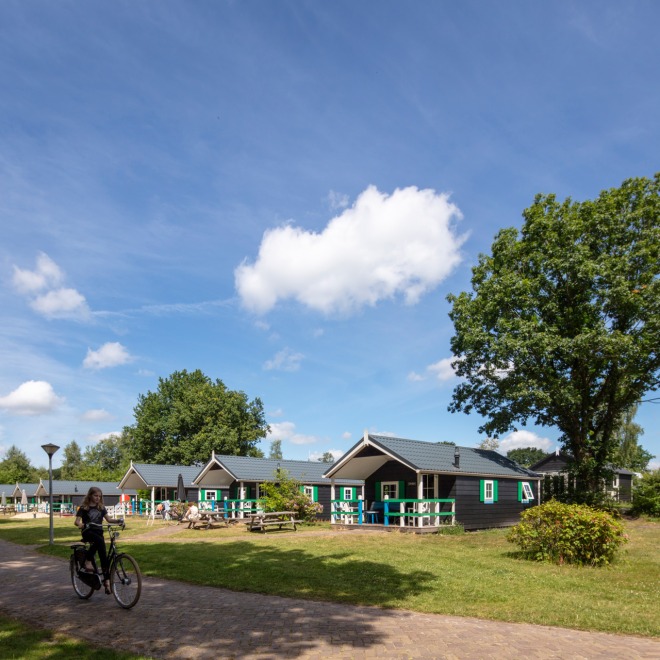 Vakantiehuizen in een groene omgeving met fietser op pad, blauwe lucht en zomerse sfeer in Nederland.