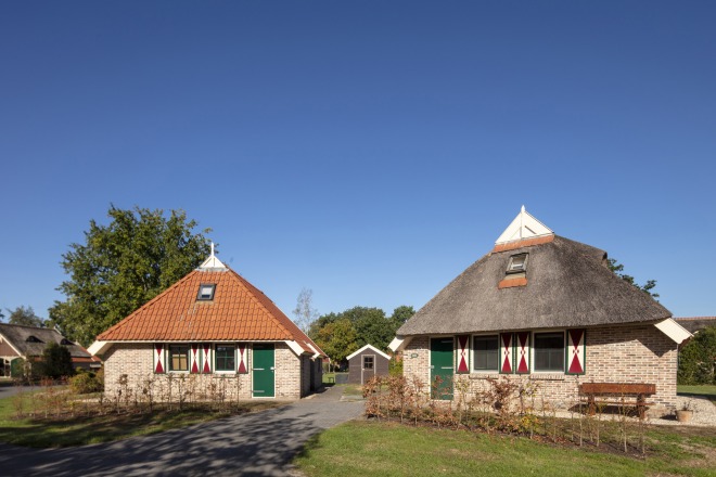 Twee traditionele Nederlandse huisjes met rieten en pannendaken, onder een heldere blauwe lucht.