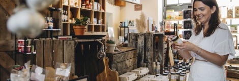 Vrouw bekijkt een product in een lokale winkel met natuurproducten, potten honing en verse eieren op tafel.