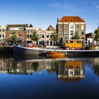 Historische grachtenpanden en woonboten weerspiegeld in het rustige water onder een heldere blauwe lucht.