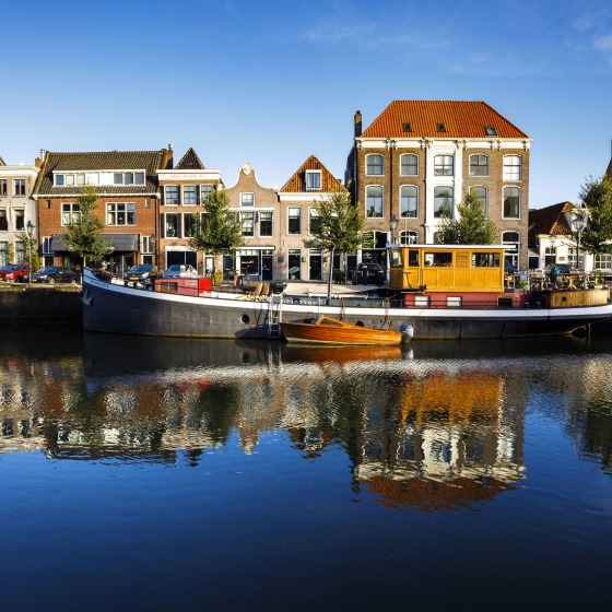 Historische Grachtenhäuser und Hausboote spiegeln sich im ruhigen Wasser unter klarem, blauem Himmel wider.