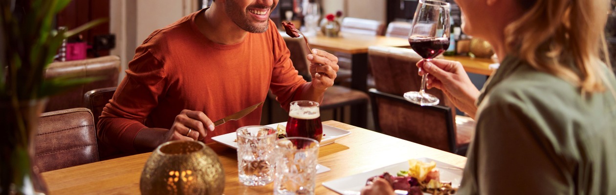 Een lachend stel geniet samen van een diner in een restaurant, met wijn en eten op tafel.