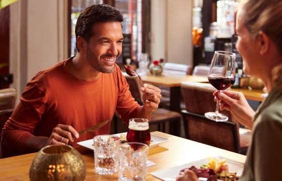 Een lachend stel geniet samen van een diner in een restaurant, met wijn en eten op tafel.