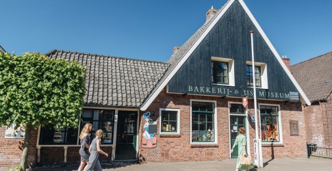 Twee vrouwen lopen langs het Bakkerij & Vis Museum in een karakteristiek Nederlands dorp.