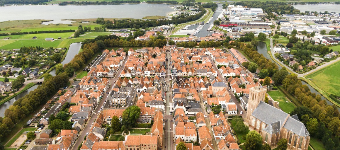 Luchtfoto van een pittoresk Nederlands stadje met rode daken, omgeven door bomen en water.