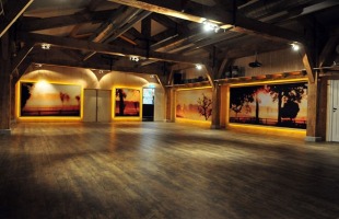 Een ruime, houten zaal met kunst aan de muur en warme verlichting die een gezellige sfeer creƫert.