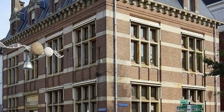 Straathoek met een historisch bakstenen gebouw, fietsenrekken, straatnaamborden en een fietser.
