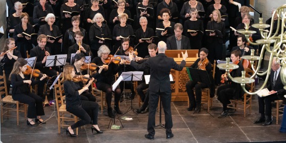 Een koor en orkest voeren een klassiek muziekstuk uit in een kerk, geleid door een dirigent.